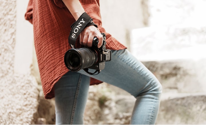 Close-up image of person carrying a camera in their right hand while casually walking up stairs with the FE 16–35 mm F2.8 GM lens mounted