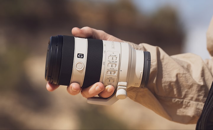 Usage image showing lens body held in palm of user's hand, emphasising compact size